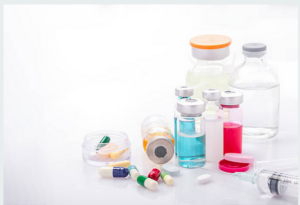 A collection of medical supplies including syringes, vials with colored liquids, capsules, and tablets on a white surface.
