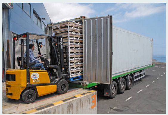 A forklift operator expertly loads large metal racks into a semi-trailer, ensuring secure transportation at the loading dock with specialized logistics.